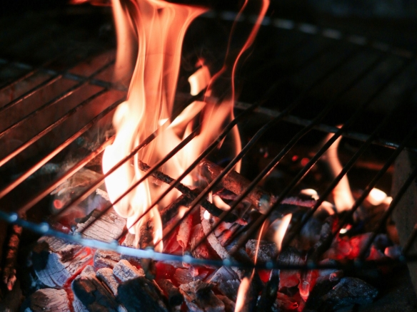 A flame over hot coals on an open barbecue