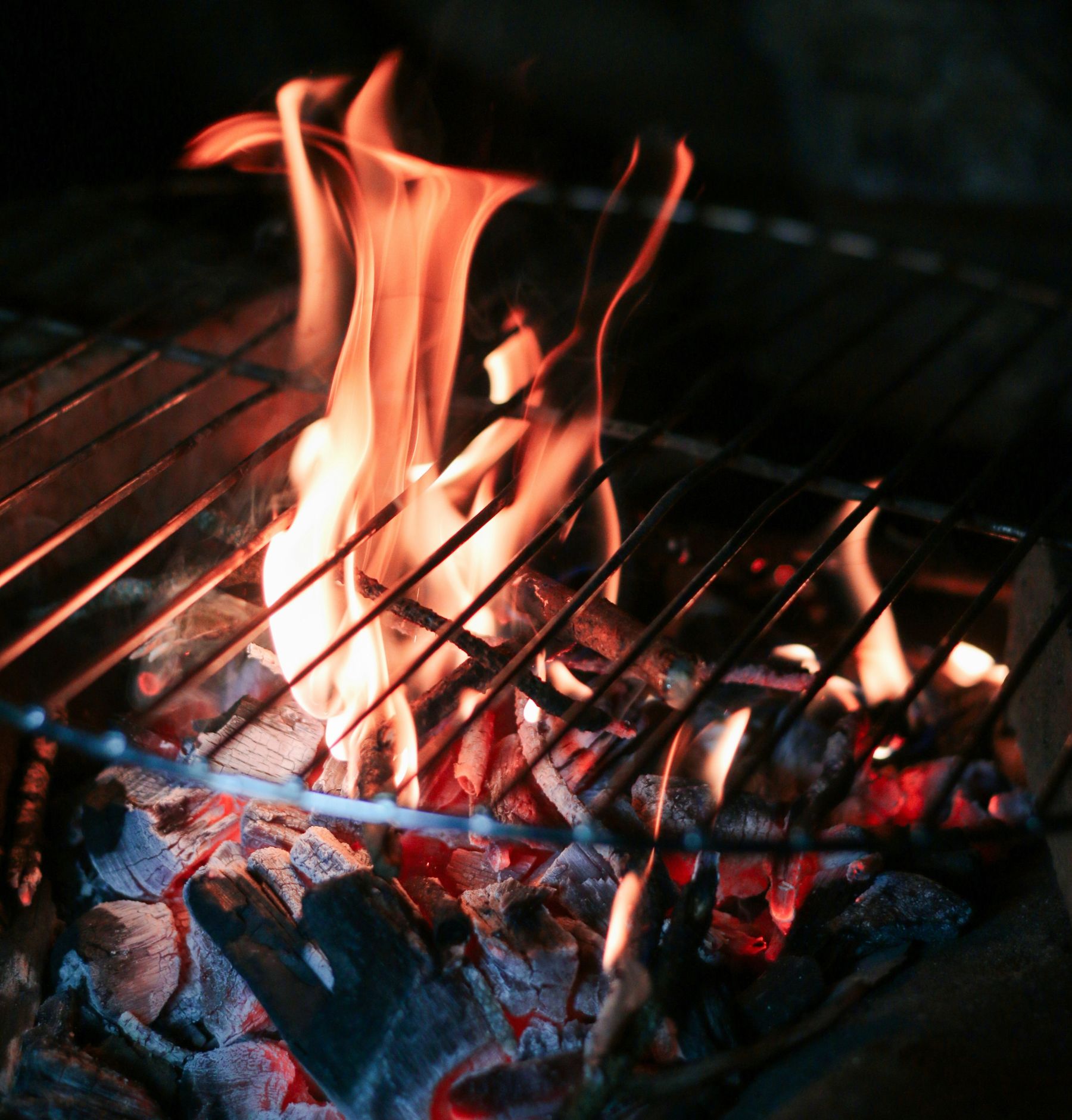 A flame over hot coals on an open barbecue